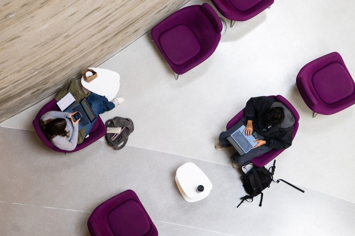 Two Northeastern students sit in purple chairs on a sleek white tile.