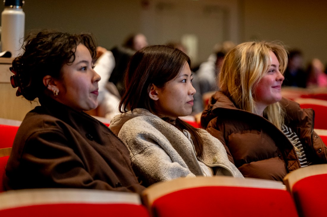 Three students sit in auditorium seats, smiline and engaged during the Husky 101 Orientation presentation at Blackman Auditorium.
