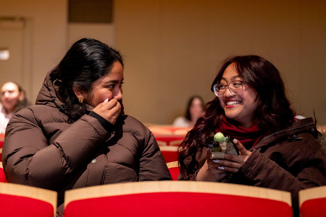 Two students laugh together during Husky 101 Orientation, one covering their mouth while laughing. 
