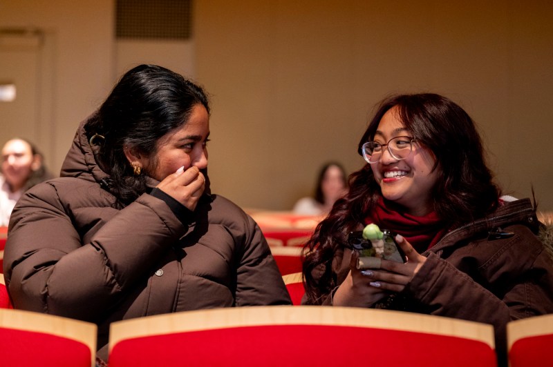 Two N.U.in smile and laugh together while seating in an auditorium. 