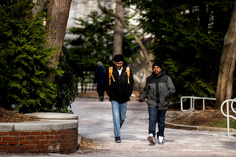 Two students walking through Bostom campus, through trees and side walks.