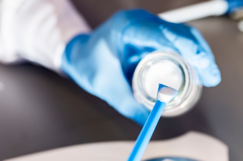 A close up photo of gloved hands using tools to scoop chemicals.