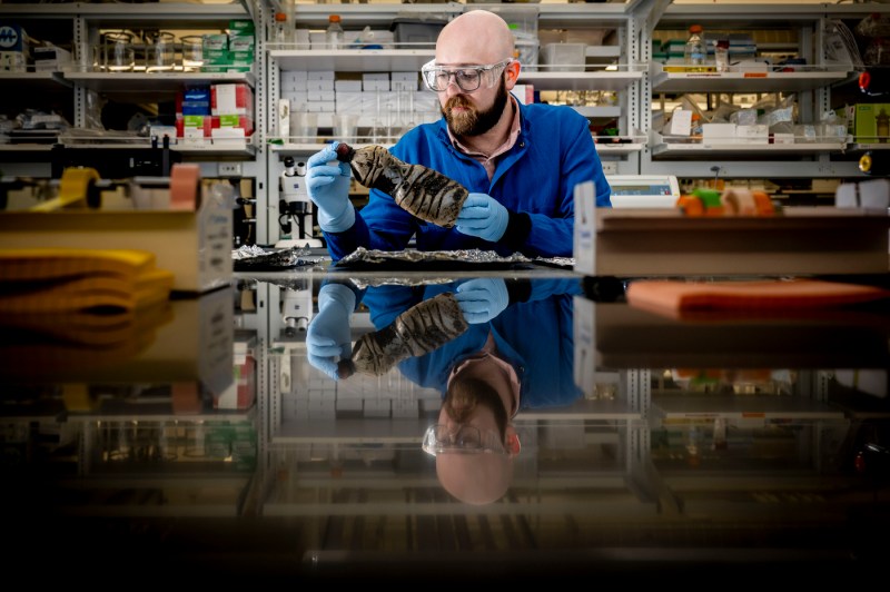 Bryan James, in a blue lab coat, works with an oil-contaminated plastic bottle in a lab.