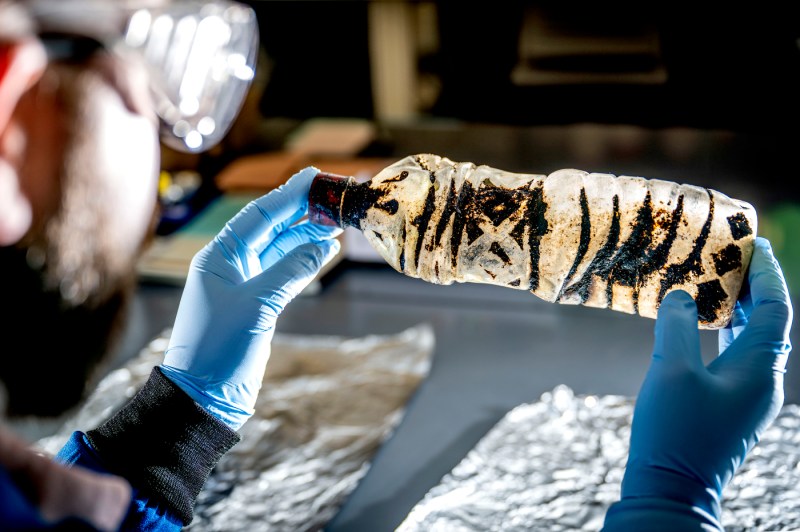 Bryan James, wearing protective goggles and latex gloves, holds a plastic bottle covered in a thick black substance.
