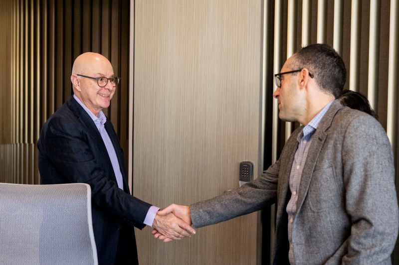 Two people shake hands inside of a university building.
