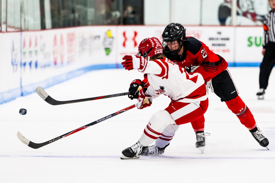 A Northeastern women's hockey player and Boston University women's hockey player battle for the puck on the ice.
