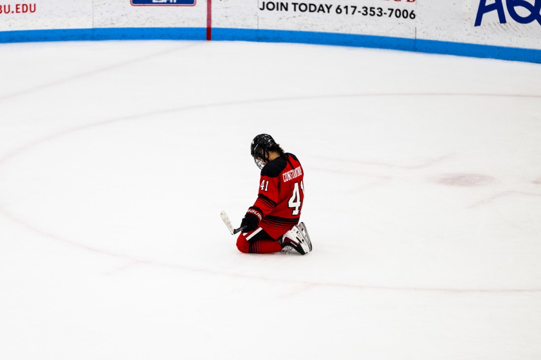 A Northeastern women's hockey player kneels on the ice with their head down, looking dejected.