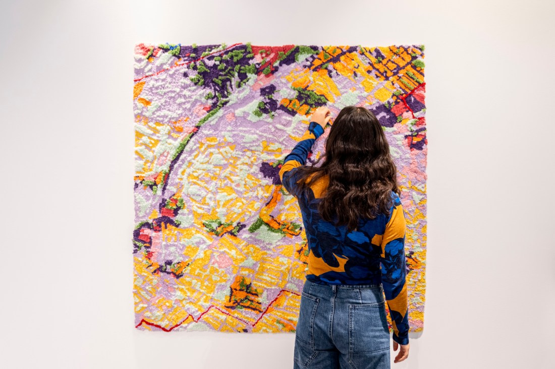 Artist Sophie Weston Chien stands in front of a large, brightly colored textile artwork used to visualize data.