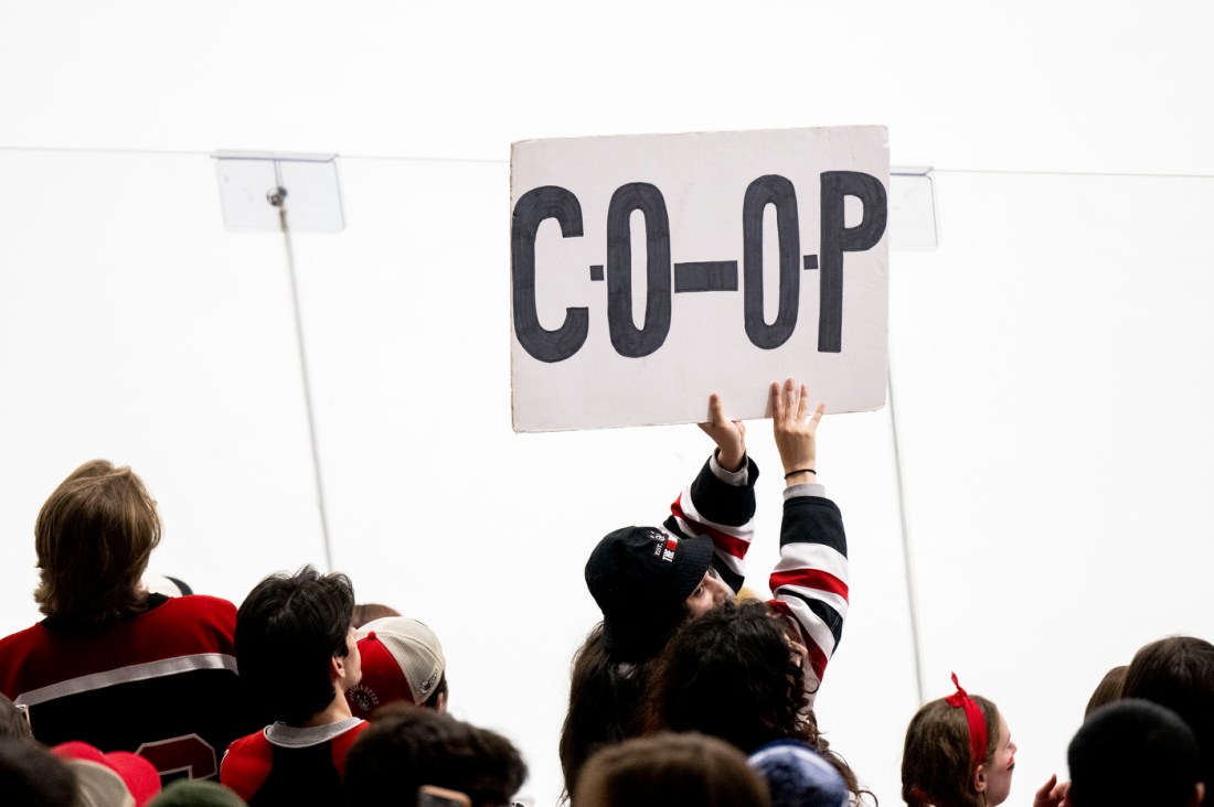 A hockey fan holds up a sign that says 'CO-OP' and looks back at the crowd over their shoulder.