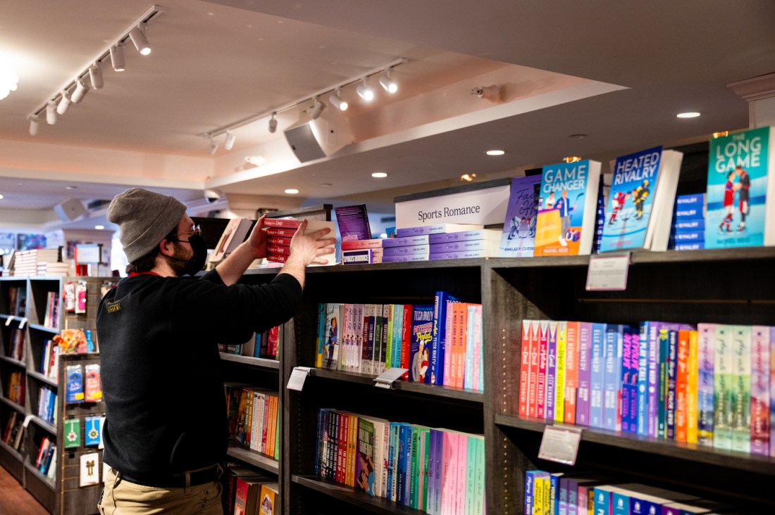 Riley Mulroy stacks and organizes books at Lovestruck Books. The bookshelf says Sports Romance.