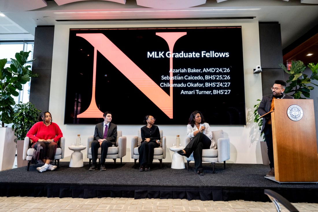 Four MLK graduate fellows students sitting on stage while Zolan Kanno-Youngs stands next to them at a podium. 