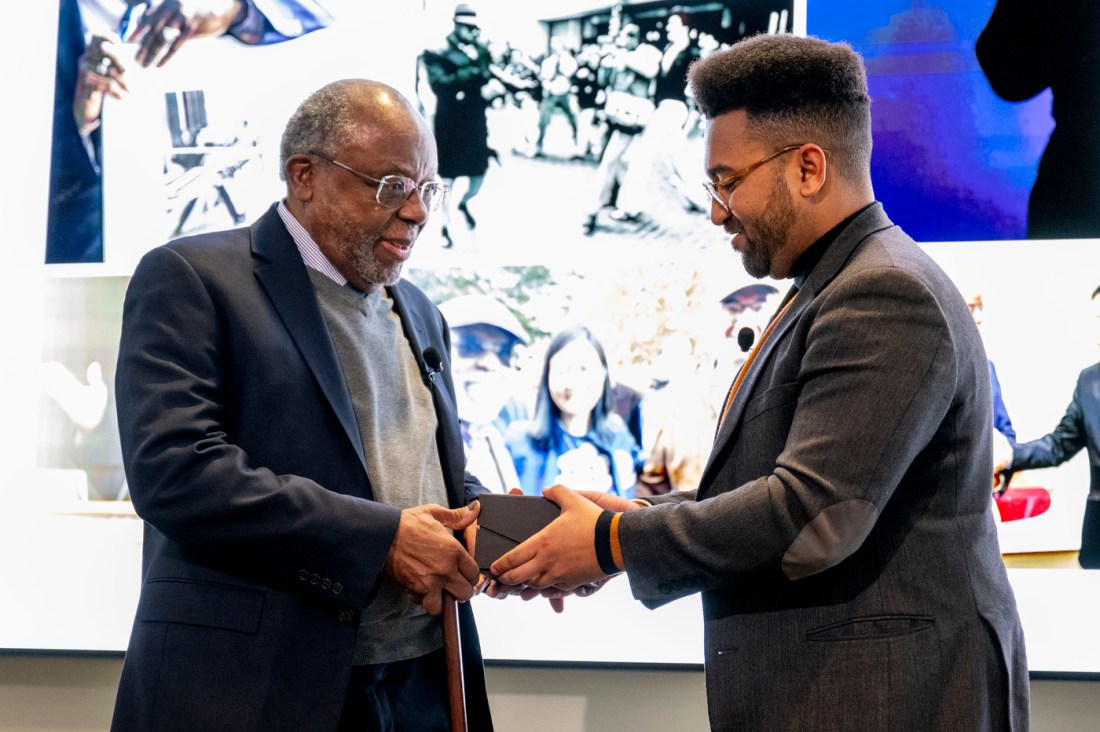 Zolan Kanno-Youngs passing a gift to Ted Landsmark on stage in the East Village 17th floor event space. 