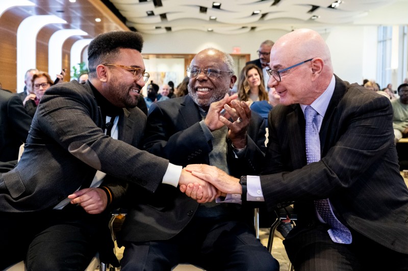 A close shot of two panelists and university president shaking hands and smiling.