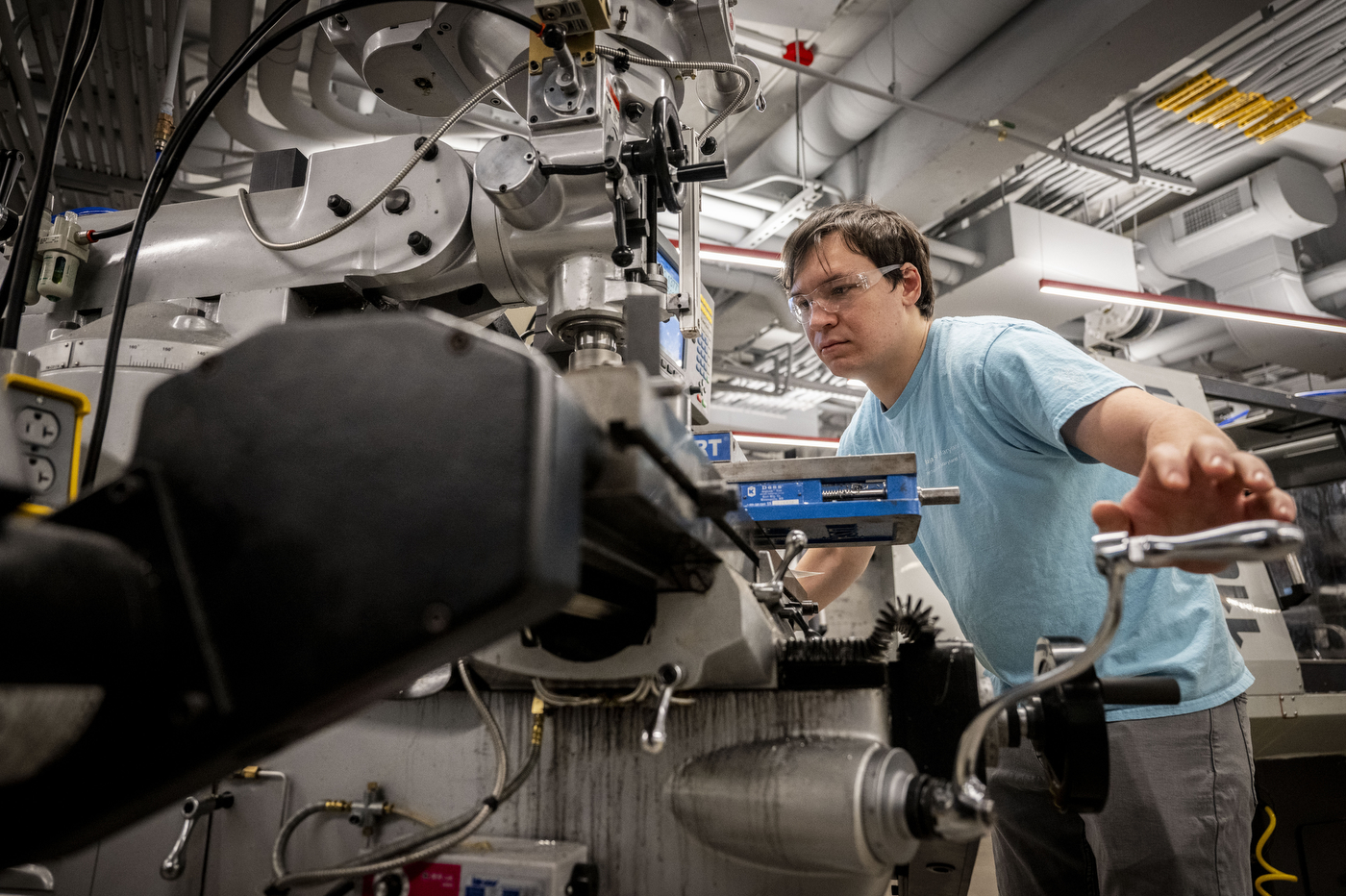 A person in safety goggles uses machinery. 