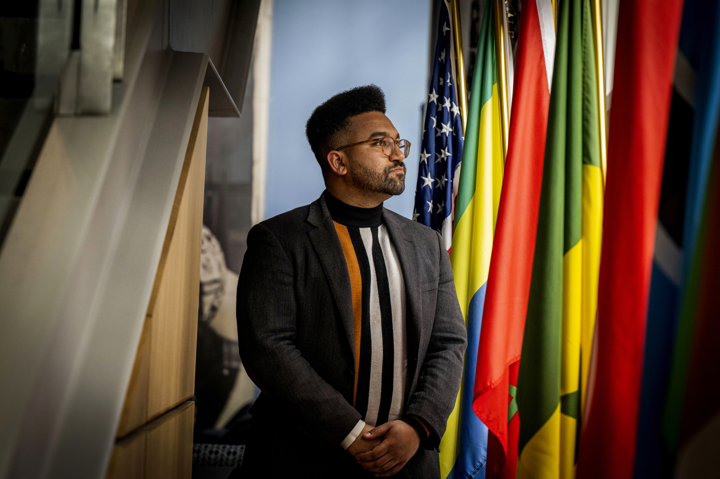 A portrait of Northeastern alumn Zolan Kanno-Youngs standing in front of multiple countries' flags.