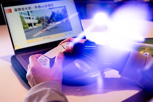 A person holds a game controller while playing on a laptop.