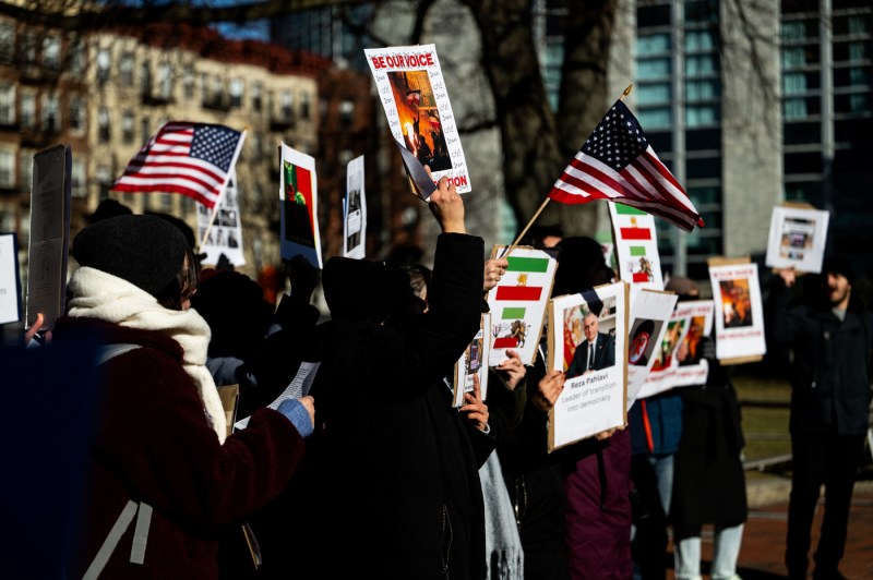 Students covering their faces hold up American flags and signs at a demonstration.