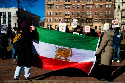 Two students with their backs turned hold the Iranian flag during a demonstration.