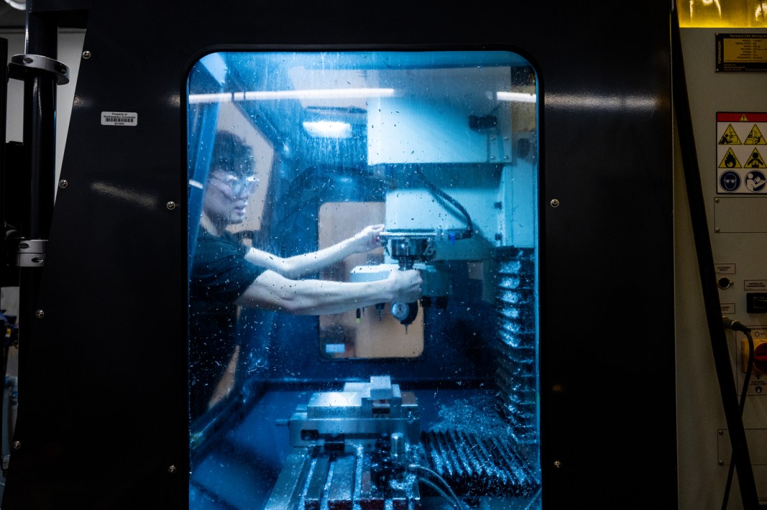 A man in a black t-shirt is pictured through the glass of a CNC Mill.
