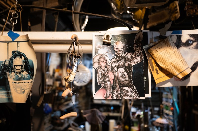Newspaper clippings and an illustration of a figure of a figure with skeleton head holding a woman by the waist hang on a line in Michael Ulman's studio.