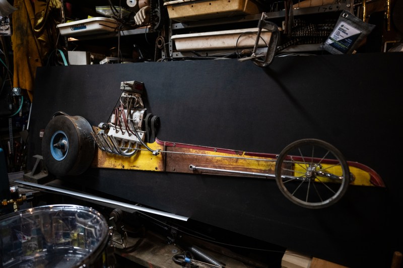 A long yellow-bodied vehicle with an exposed engine hangs against a black background in Michael Ulman's studio.