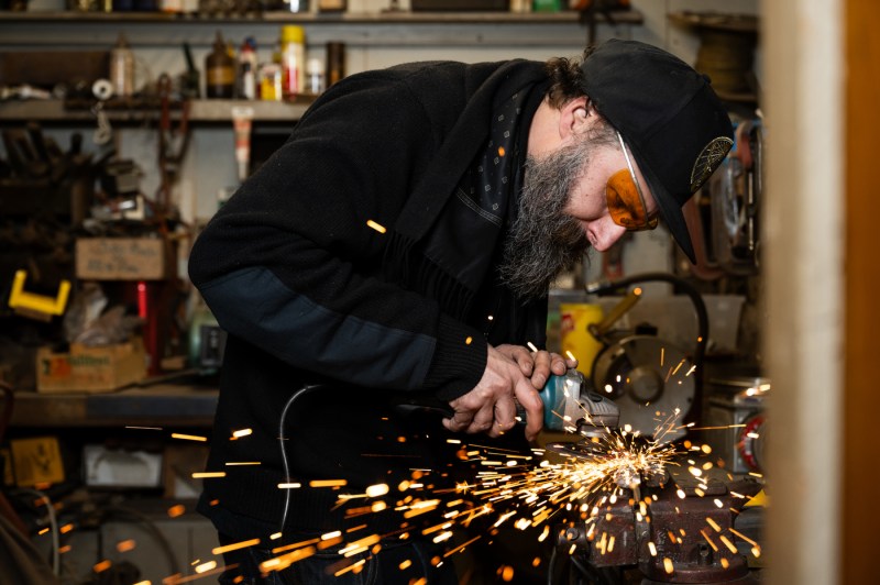 A sculptor welds together metal while wearing safety goggles.