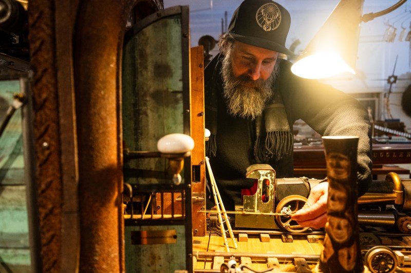 A sculptor works on a new art piece with assorted recycled objects on a work table.