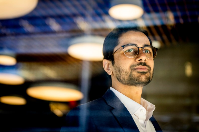 An assistant professor looks off to the right with reflections of light fixtures around his face, posing for a portrait.