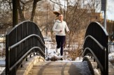 Lily Poteet wearing black leggings, white sneakers and a white zip-up sweater running over a bridge in an urban park.