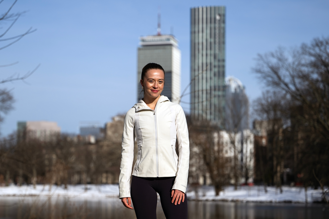 A student in running gear poses for a portrait with snow-covered buildings in the background.