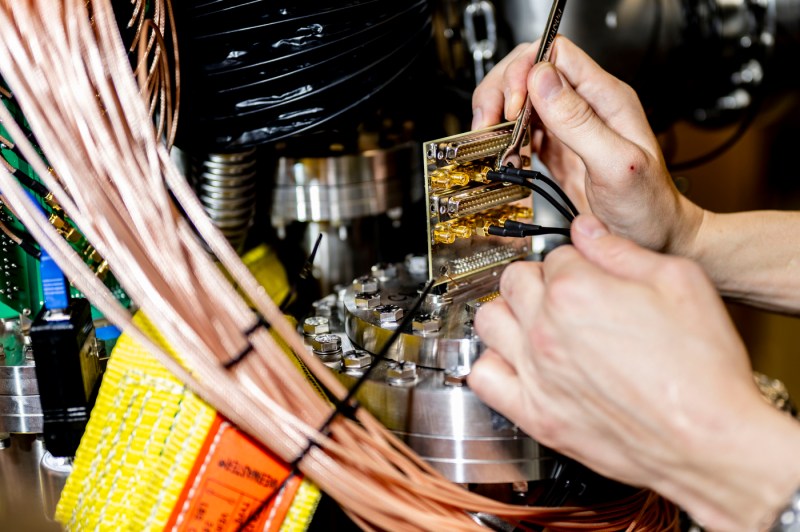 Two hands use delicate tools to work with equipment and wiring.