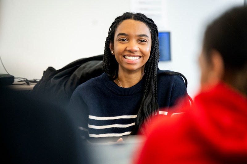 A postdoc student smiles for a portrait while sitting in a classroom.
