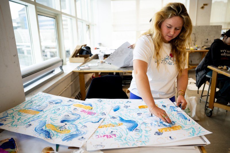 A person leans over a table while painting.