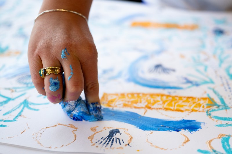 Close up of a hand covered in blue paint while painting on a large piece of paper.