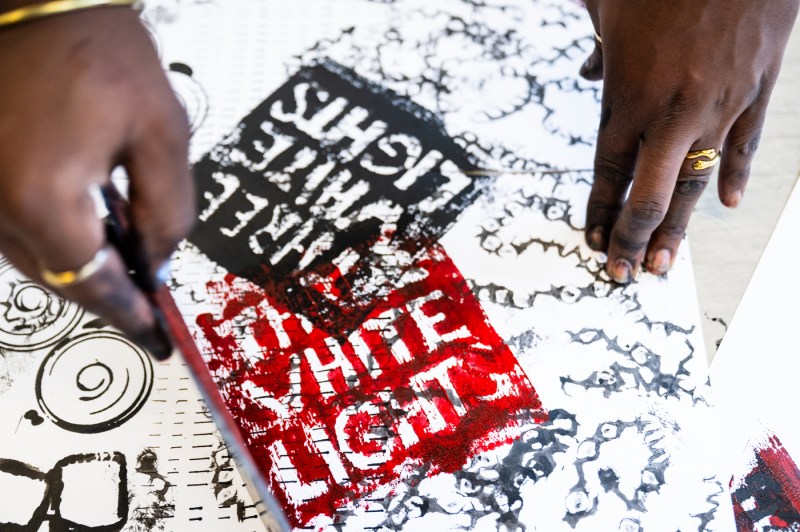A close up of two hands using a stamp to paint on a large sheet of paper.