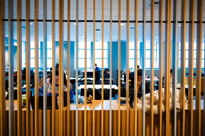 Students studying in a community building sit behind a wall of wooden panels.
