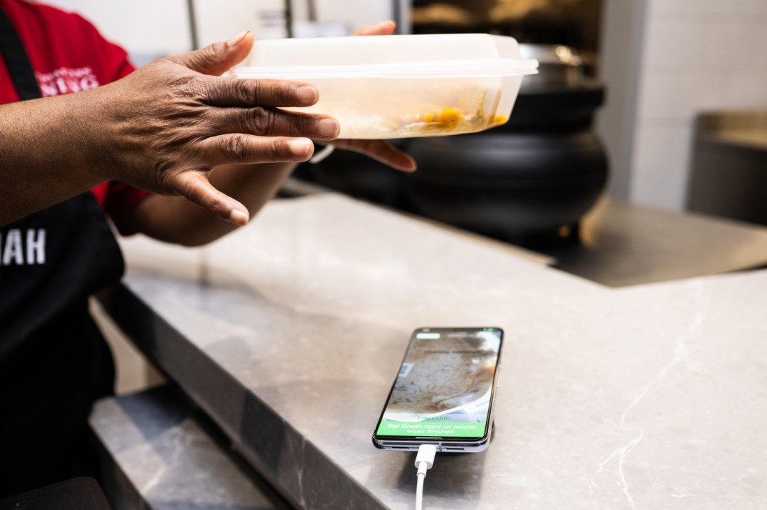 Close-up of hands exchanging a takeout container across a counter, with a smartphone charging on the counter surface