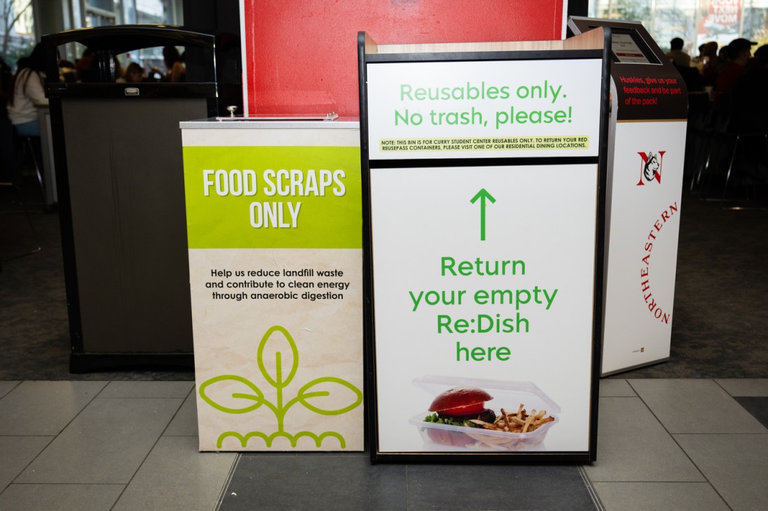 Two waste management stations side by side: a green 'Food Scraps Only' composting bin and a white sign reading 'Return your empty Re:Dish here' with reusable containers pictured, part of a campus sustainability program.
