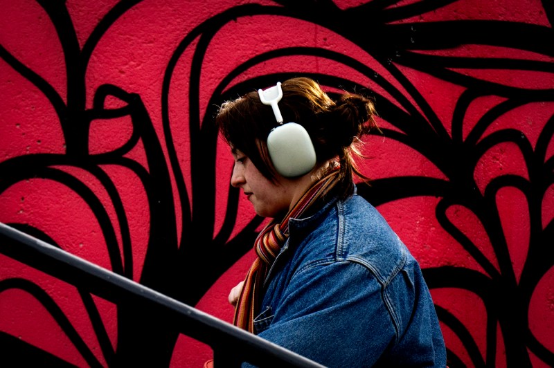 A student wearing headphones walks past a wall with a bright red mural.