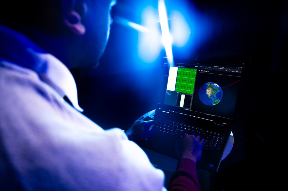 A man looks at his laptop while a blue light is faced in front of him. 