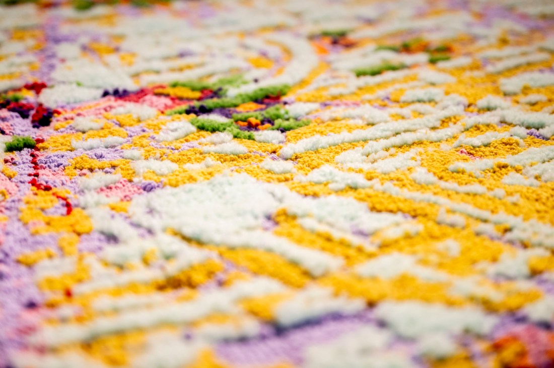 A close-up of a tufted textile artwork with raised patterns in yellow, white, purple, green and pink, used to visualize data. 