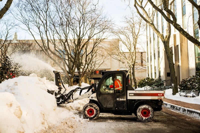 A facilities worker operates heavy machinery to plow snow on campus.