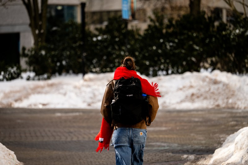 The back of a student wearing a large backpack as they trek through the snow-covered Boston campus.