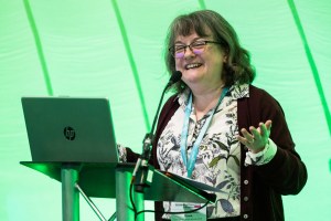 Woman at podium holding up a laptop