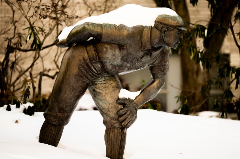 Snow covers a statue of a baseball player.