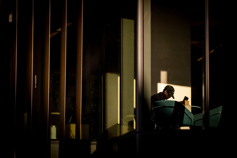 A person sits with their laptop in the strong, shadowy ISEC building.