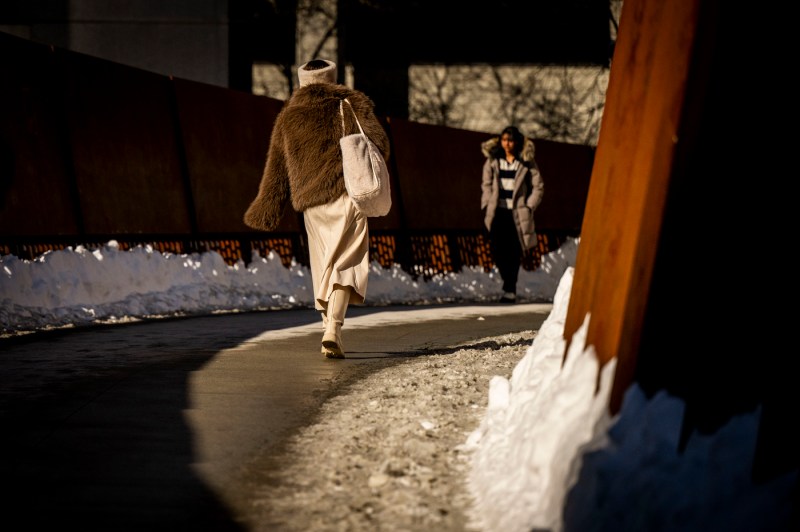 A student dressed in a brown coat crosses the pedestrian brdige.
