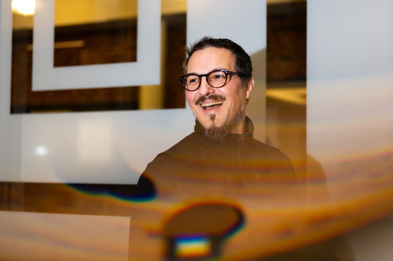 A person with glasses and wearing all black smiles while looking to the left.