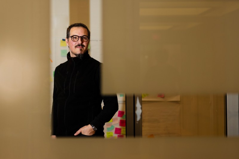 A person with glasses and wearing all black poses for a portrait while looking to the right.