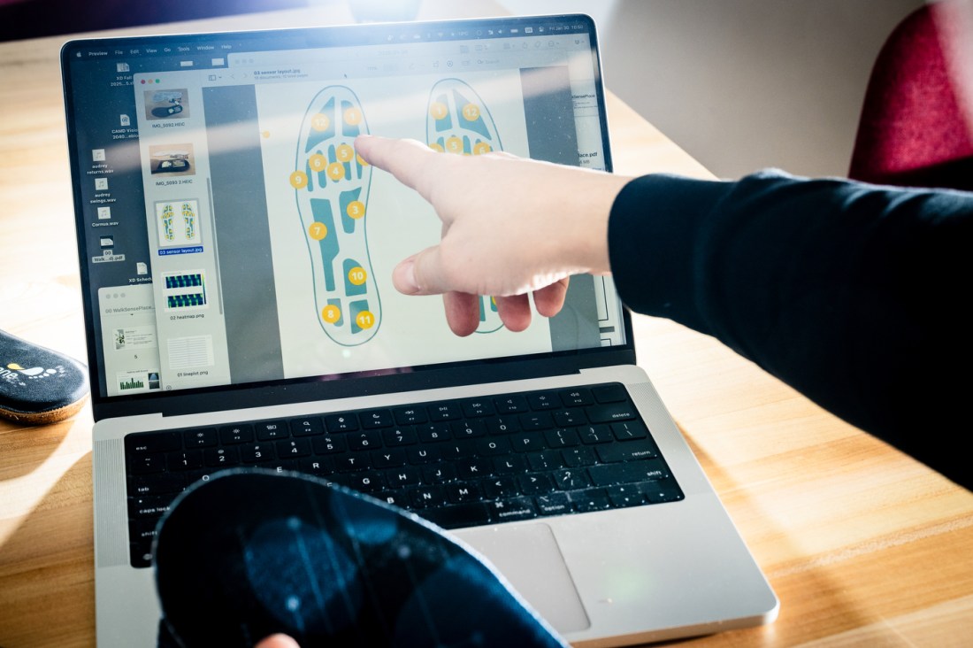 A hand points to a computer screen with an image of the insole and twelve numbered sensors.